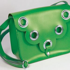 May include: A bright green shoulder bag featuring a scalloped flap closure adorned with five large silver-toned metal eyelets. The bag includes a matching green shoulder strap attached with a silver-toned metal ring and a snap button closure.