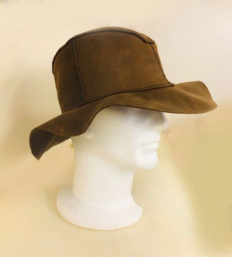 Puede incluir: Un sombrero de gamuza marr&oacute;n de ala ancha con un ala ca&iacute;da. El sombrero est&aacute; en una cabeza de maniqu&iacute; blanca.