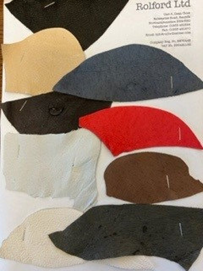 May include: A selection of fabric swatches in diverse colours such as black, beige, navy, red, brown, and white. Each swatch has a unique shape and size, with pins attached. The swatches are arranged on a white background with text at the top.