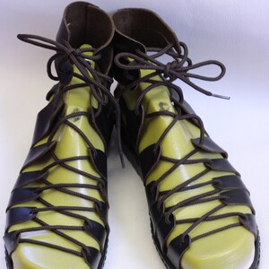 May include: A pair of brown leather sandals with a green insole and brown laces. The sandals have a strap that goes around the ankle and laces that tie up the front.