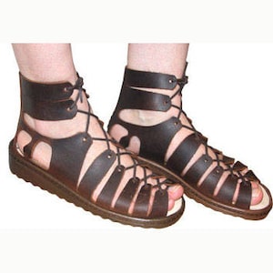 May include: Brown leather gladiator sandals with laces that tie up the leg. The sandals have a flat sole and are open-toed.