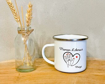 May include: White enamel mug with a black and red design that says "Maman d'Amour" and "Margot". The mug has a silver rim and a handle.