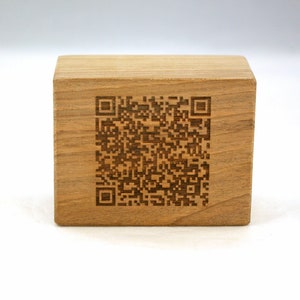Pode incluir: Um bloco de madeira com um código QR preto e branco gravado na frente.