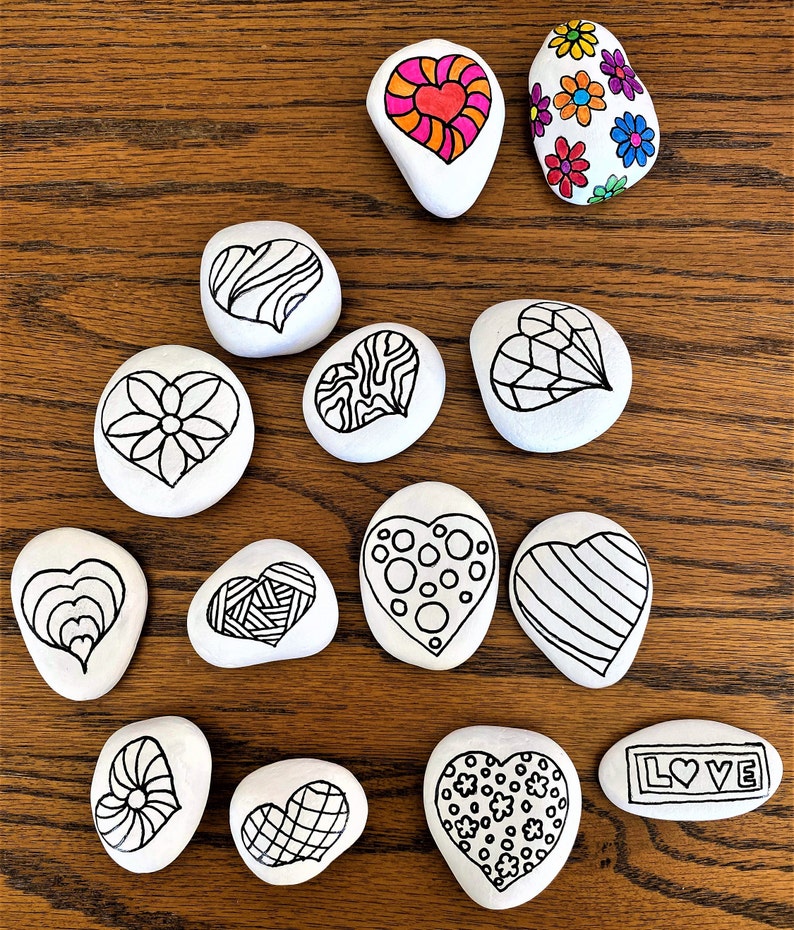 Pu&ograve; includere: Una collezione di 13 pietre dipinte a forma di cuore. Le pietre sono dipinte con vari disegni, tra cui strisce, pois, fiori e motivi geometrici. Una pietra ha la parola "LOVE" scritta su di essa.