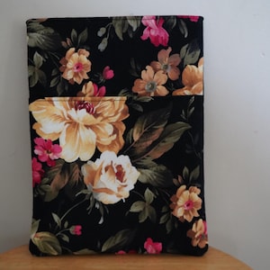 May include: A rectangular fabric case with a floral pattern. The case features large yellow and white flowers, pink buds, and green leaves against a black background. The case is likely designed to hold a tablet or other electronic device.