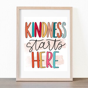 May include: A framed print with the text "Kindness starts here" in colorful, handwritten letters on a pink and white background.