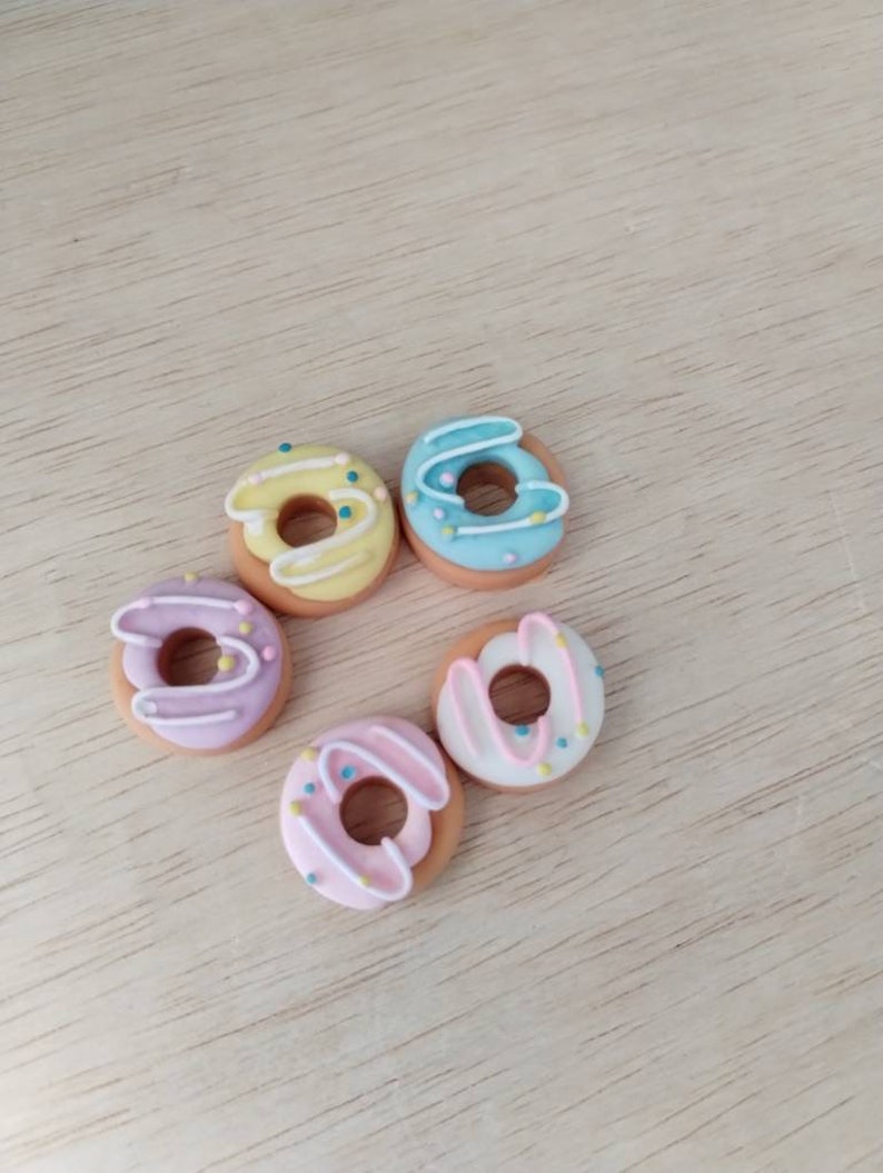 May include: Five miniature donuts with different colored glazes and sprinkles. The donuts are arranged in a circle on a light wood surface.