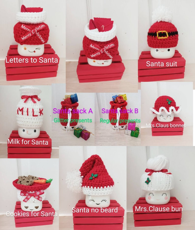 Op de afbeelding: Negen verschillende gehaakte bekertoppers, elk met een ander kerstthema. De toppers zijn gemaakt van wit en rood garen en hebben verschillende ontwerpen, waaronder kerstmanmutsen, melkpakken en koekjes. De toppers worden gepresenteerd op rode houten kisten.