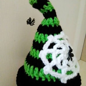 May include: A black and green crocheted witch hat with a white crocheted spider web design and two black plastic spiders.