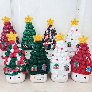 May include: Six white ceramic mugs with crocheted Christmas tree hats. The hats are in various colors and patterns, including red, green, white, and candy cane stripes. Each mug has a smiling face.