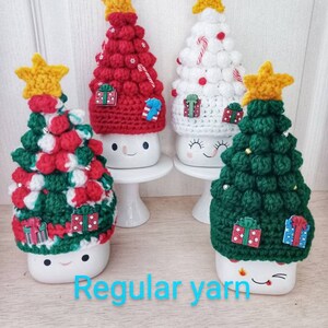 May include: Four crocheted Christmas tree mug toppers in red, white, and green with a yellow star on top. Each topper has a white mug underneath with a happy face.