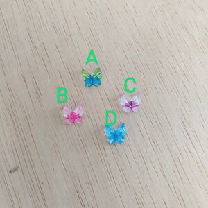 Op de afbeelding: Vier kleurrijke vlinderversieringen op een houten oppervlak. De vlinders zijn in tinten blauw, roze en groen.