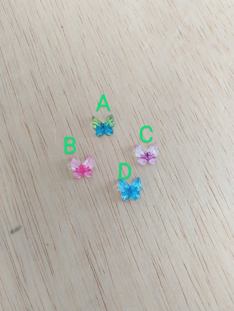 Op de afbeelding: Vier kleurrijke vlinderversieringen op een houten oppervlak. De vlinders zijn in tinten blauw, roze en groen.