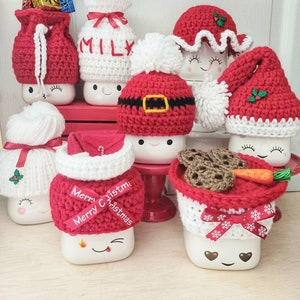 Op de afbeelding: Set van zeven witte keramische mokken met rood-witte gehaakte mutsen. De mutsen hebben verschillende kerstthema's, waaronder Sinterklaas, een melkpak, een sneeuwpop en een rendier. De mokken hebben schattige cartoongezichten en zijn perfect voor warme chocolademelk of andere winterdrankjes.