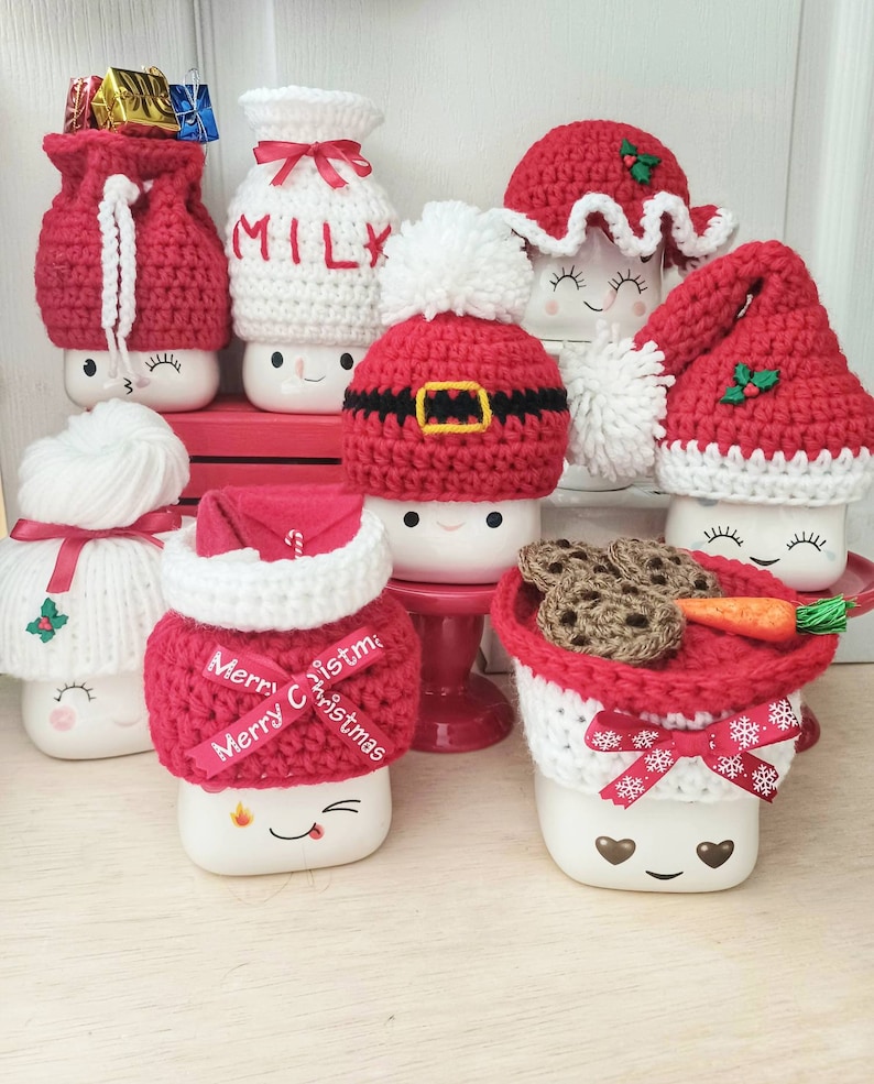 Op de afbeelding: Set van zeven witte keramische mokken met rood-witte gehaakte mutsen. De mutsen hebben verschillende kerstthema's, waaronder Sinterklaas, een melkpak, een sneeuwpop en een rendier. De mokken hebben schattige cartoongezichten en zijn perfect voor warme chocolademelk of andere winterdrankjes.