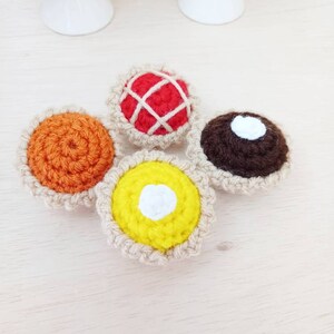 May include: Four crocheted mini pies with different fillings: orange, red, brown, and yellow. Each pie has a white crocheted crust.