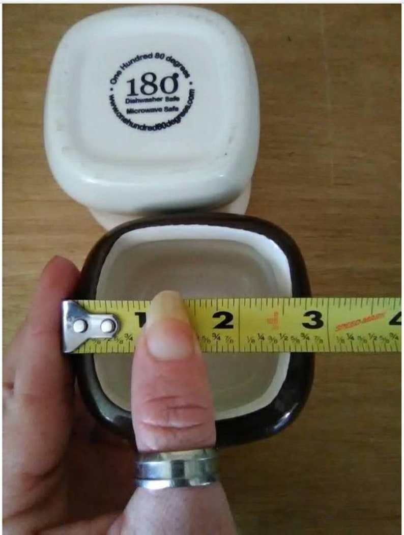 May include: A brown and white ceramic ramekin with a white rim. The ramekin is 2 inches in diameter. The ramekin has the words "One Hundred 80 degrees" and "180" printed on the bottom.