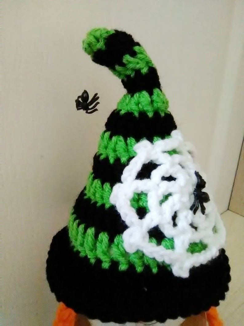 May include: A black and green crocheted witch hat with a white crocheted spider web design and two black plastic spiders.