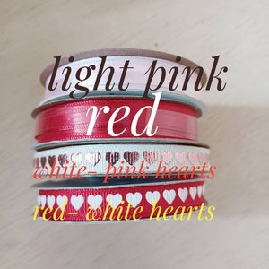 May include: Four spools of ribbon in different colors and patterns. The top spool is light pink, the second is red, the third is white with pink hearts, and the bottom is red with white hearts.