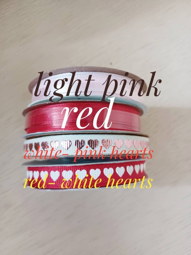 May include: Four spools of ribbon in different colors and patterns. The top spool is light pink, the second is red, the third is white with pink hearts, and the bottom is red with white hearts.