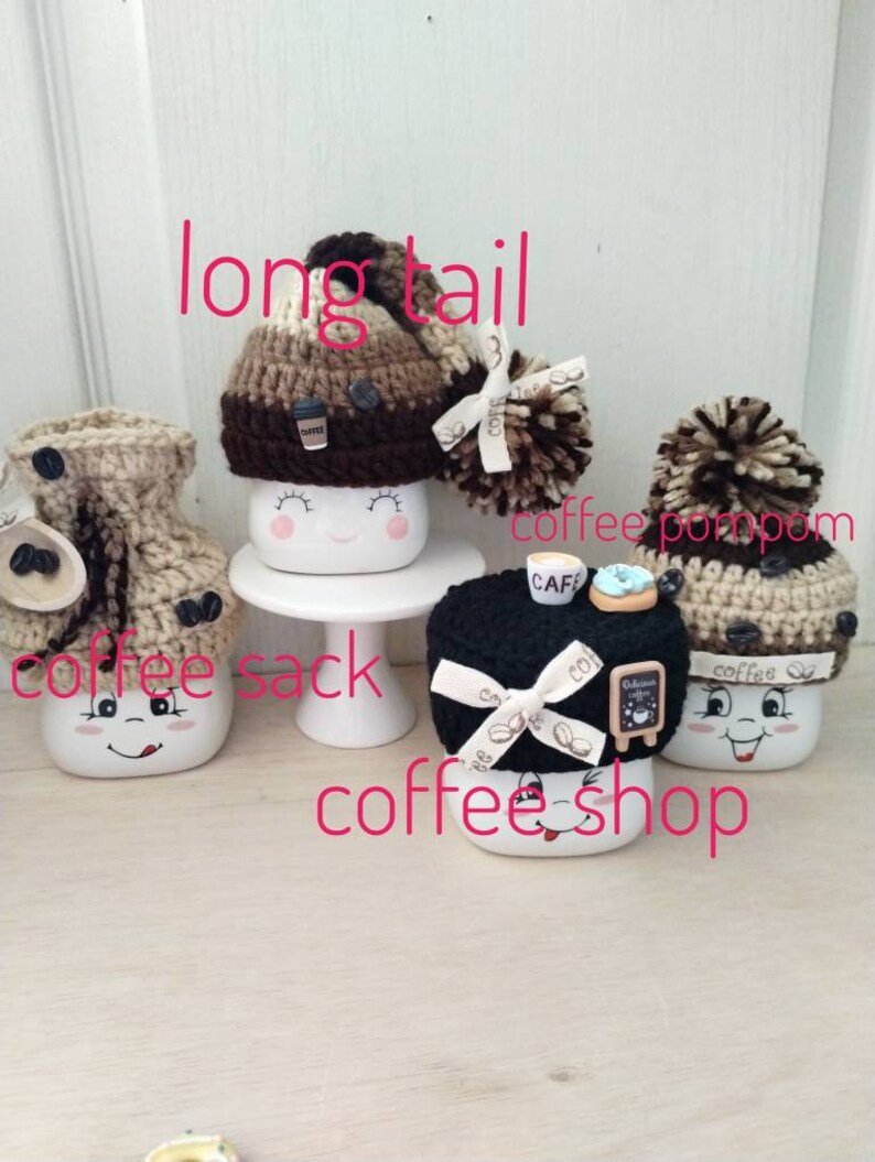 May include: Four white ceramic mugs with different knitted hats. The mugs have a smiling face and are decorated with coffee-themed details. The hats are brown, black, and beige with pom-poms. The text "coffee sack" and "coffee shop" are written on the image.