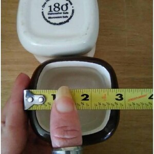May include: A brown and white ceramic ramekin with a white rim. The ramekin is 2 inches in diameter. The ramekin has the words "One Hundred 80 degrees" and "180" printed on the bottom.