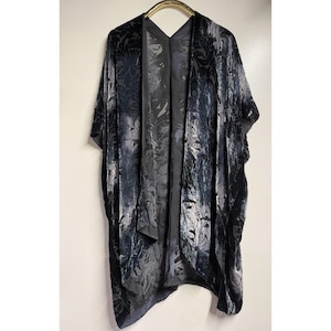 May include: A dark gray and black velvet kimono featuring an intricate, tonal floral pattern throughout the fabric. This open-front garment has wide, loose sleeves and a draped, flowing silhouette that hangs straight down from the shoulders.