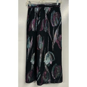May include: Black wide-leg pants with a metallic tulip floral pattern in shades of purple, teal, and silver. The pants are hanging on a hanger against a white background. The waistband is elastic.