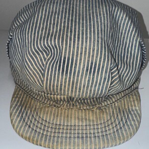 May include: A blue and white striped cap with a rounded crown and a short, curved brim. The cap has vertical stripes and appears to be made of a worn fabric. The brim shows signs of wear and discoloration.
