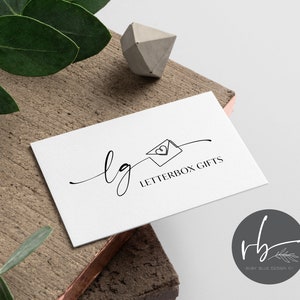 Puede incluir: Una tarjeta de visita blanca con el texto "lg LETTERBOX GIFTS" en una escritura negra minimalista. La tarjeta está sobre una superficie de madera con un adorno geométrico de hormigón y hojas verdes.