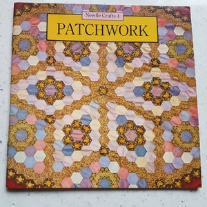 Peut inclure: Une couverture de livre avec le titre "PATCHWORK" en lettres jaunes sur un fond jaune. Le livre fait partie d'une série intitulée "Needle Crafts 4". La couverture présente un motif de courtepointe patchwork coloré avec des formes hexagonales dans des tons de rose, violet, bleu et jaune.