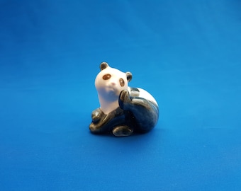 May include: A ceramic panda figurine with black and white fur, sitting on a blue background.
