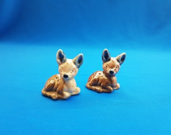 以下が含まれることがあります： 青い背景に置かれた、茶色と白の小さな陶器製の鹿の置物2つ。茶色の斑点がある。