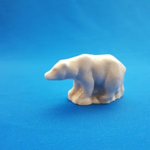 May include: A white ceramic polar bear figurine. The bear is sitting on its haunches with its head turned to the left. The figurine is on a blue background.