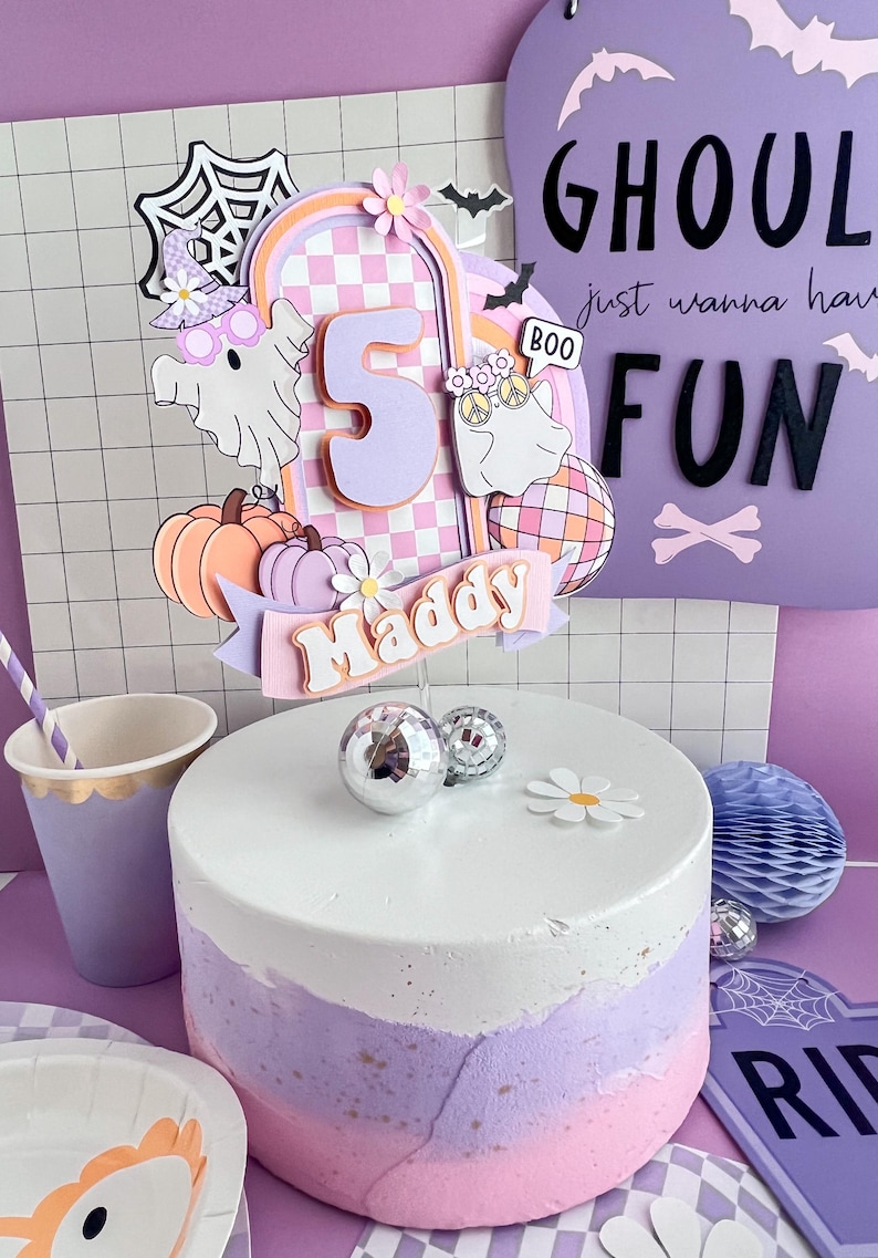 May include: A layered cake topper featuring a large number 5, a banner with the name Maddy, two ghosts, pumpkins, a disco ball, and a spiderweb. The design uses pastel colors including pink, purple, and orange with a checkered arch background.