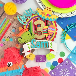 May include: A colorful fiesta themed cake topper with a sombrero, cactus, maracas, and the number 3. The topper also includes the name Sam and the word "fiesta".