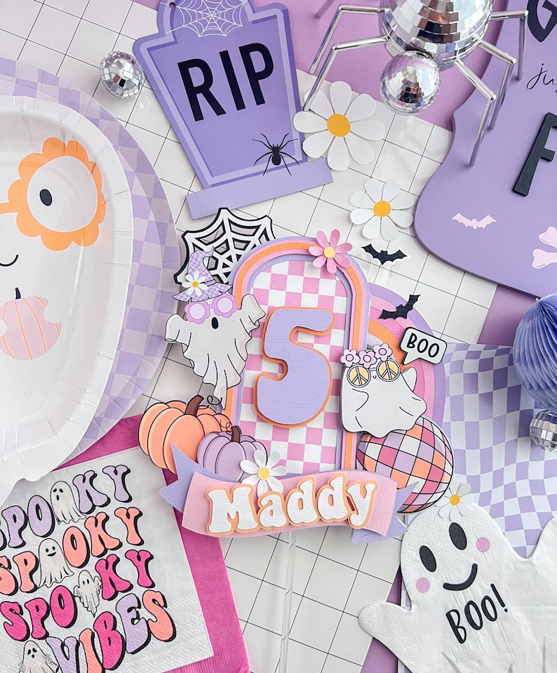 May include: A layered paper cake topper featuring the number 5 in orange, a checkered arch, two ghosts, pumpkins, a disco ball, and a banner with the name Maddy. The design includes pastel purple, orange, and white colors with floral accents.