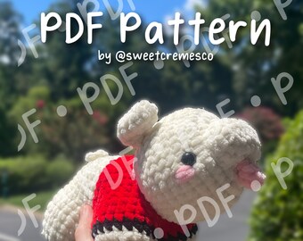 May include: A white crocheted plush toy wearing a red and black crocheted sweater. The toy is being held by a hand. The image includes the text "PDF Pattern by @sweetcremesco" and "PATTERN DOWNLOAD ONLY *NOT* A PHYSICAL PLUSHIE".