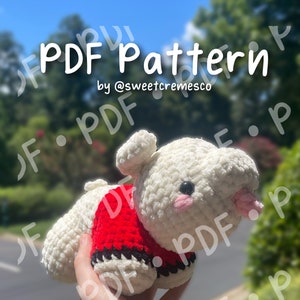Puede incluir: Un juguete de peluche blanco tejido a crochet con un suéter tejido a crochet rojo y negro. El juguete está siendo sostenido por una mano. La imagen incluye el texto "PDF Pattern by @sweetcremesco" y "PATTERN DOWNLOAD ONLY *NOT* A PHYSICAL PLUSHIE".