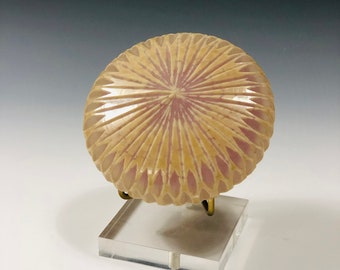 May include: A round, ceramic dish with a pink and cream glaze. The dish has a raised, geometric pattern that resembles a flower.