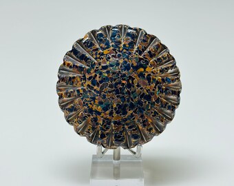 May include: A round, decorative object with a textured surface. The object is made of a dark blue and brown material with a speckled pattern. It is displayed on a clear stand.