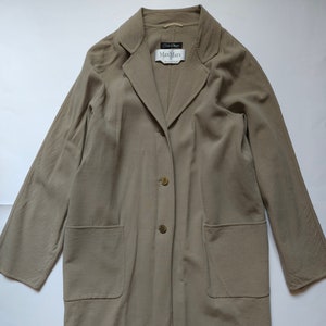 Op de afbeelding: Een lange, beige Max Mara jas met knoopsluiting en twee klepzakken. De jas heeft een klassieke, getailleerde uitstraling.
