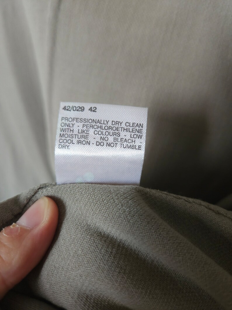 Op de afbeelding: Een wit waslabel met de tekst "Professionally dry clean only - Perchloroethylene with like colours - Low moisture - No bleach - Cool iron - Do not tumble dry" en de nummers "42/029 42".
