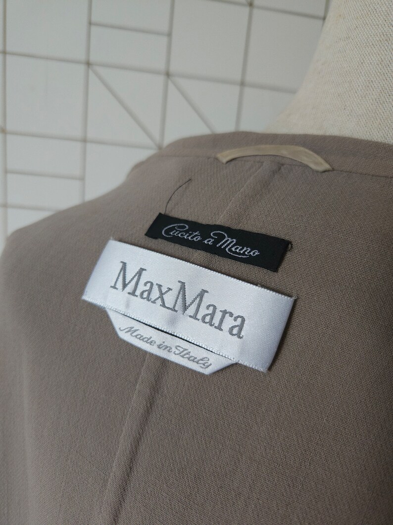 Op de afbeelding: Een bruine Max Mara blazer met een wit label waarop "Max Mara" en "Made in Italy" staat. Het label heeft ook een kleiner zwart label met de tekst "Cucito a Mano".