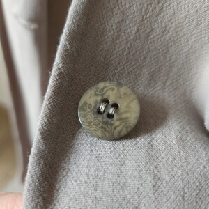 Op de afbeelding: Een close-up van een bruine knoop met een marmerpatroon op een beige stoffen achtergrond.