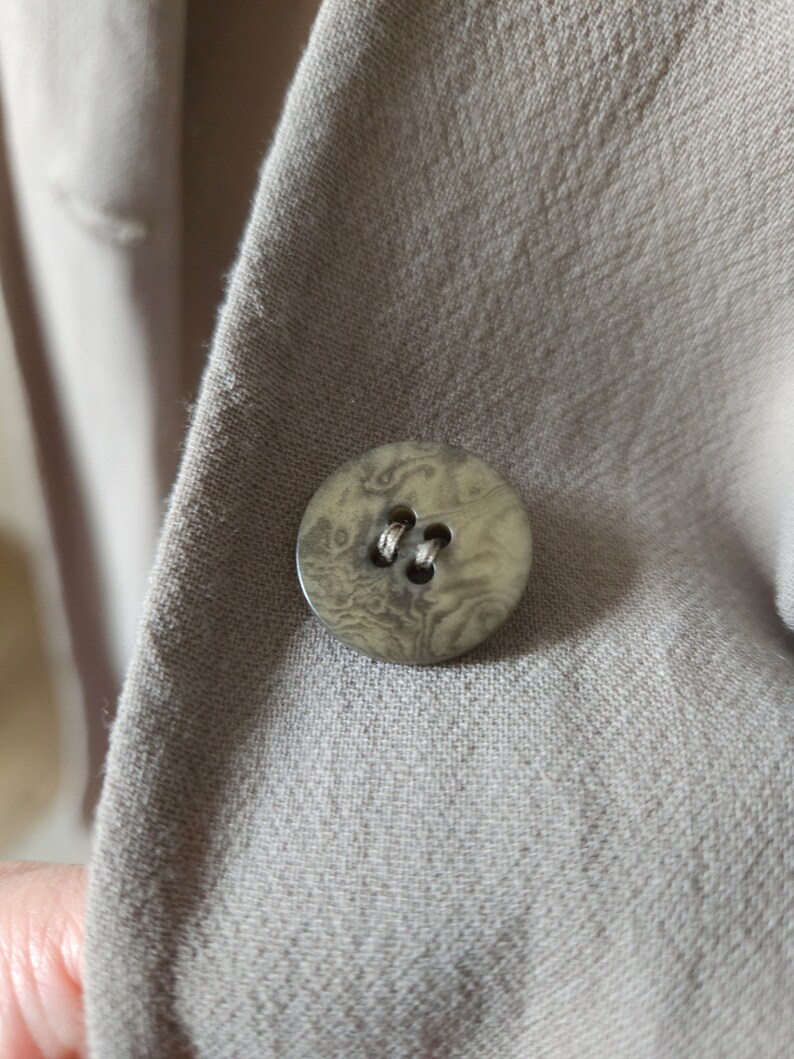 Op de afbeelding: Een close-up van een bruine knoop met een marmerpatroon op een beige stoffen achtergrond.