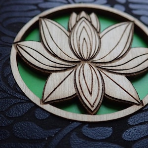 May include: A wooden cutout of a lotus flower with a green background. The flower is intricately carved and has a natural wood finish.