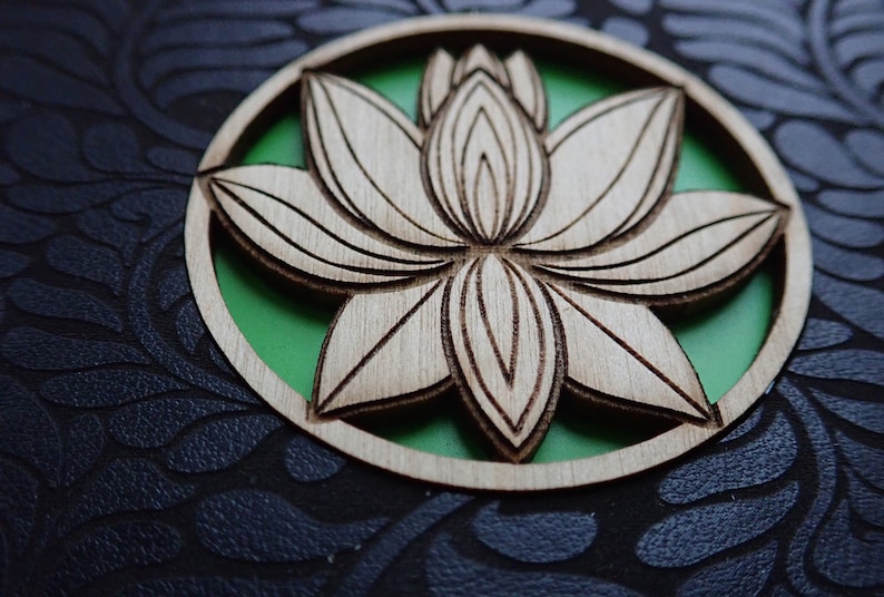 Puede incluir: Un recorte de madera de una flor de loto con un fondo verde. La flor est&aacute; tallada de forma intrincada y tiene un acabado de madera natural.