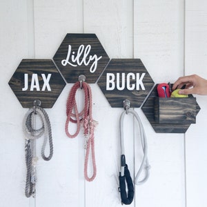 May include: A wooden dog leash holder with three hexagon-shaped hooks and a small storage compartment. The hooks are labeled "Jax", "Lilly", and "Buck".