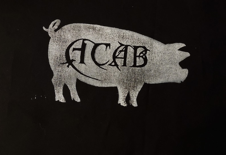 K&ouml;nnte beinhalten: Eine wei&szlig;e Silhouette eines Schweins mit den Buchstaben "ACAB" innerhalb der Silhouette auf schwarzem Hintergrund.